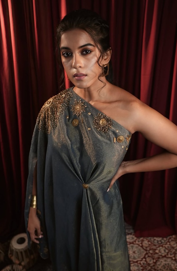 A woman wearing an elegant dark grey and gold one-shoulder cape dress by Anahita Shelat, showcasing versatile styling in investment dressing Indian fashion.